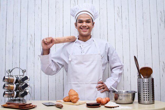 Happy male Asian chef or baker in toque holding rollingpin