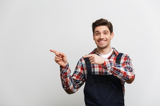 Happy male builder pointing away with two forefingers  over grey wall