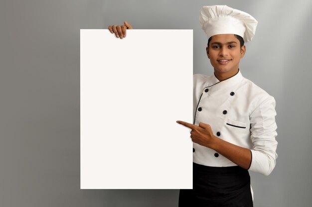 Happy male chef dressed in uniform holding white advertising banner good poster for ad