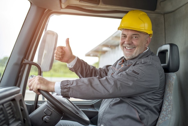 햇빛 아래 트럭에서 엄지손가락을 위로 올리는 제스처를 하는 행복한 남성 건설 노동자