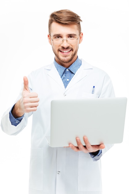 Happy male doctor holding laptop computer and showing thumb up isolated on a white background