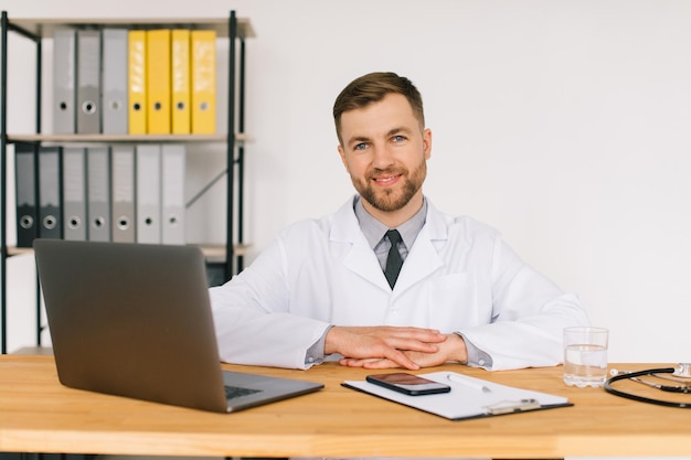 Happy male doctor watching an online medical webinar or\
training seminar while sitting with a laptop in the workplace