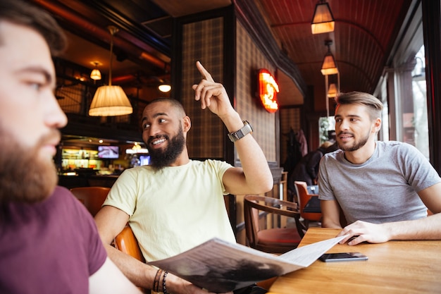 Счастливые друзья-мужчины звонят официанту для того, чтобы сделать заказ в ресторане