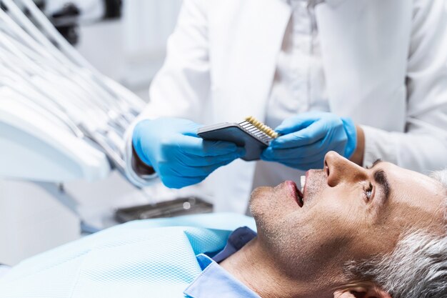 Happy male is lying in dental chair while doctor is treating hit teeth before whitening