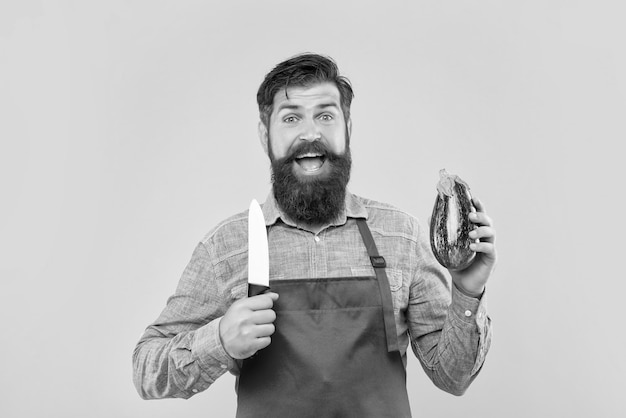 Счастливый мужчина в фартуке держит поварской нож и баклажан на желтом фоне повара