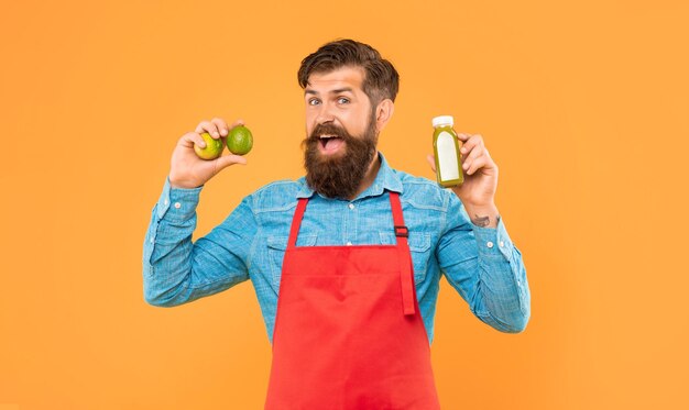 happy man in apron holding limes and juice bottle yellow background juice barman