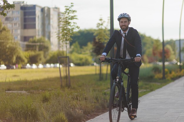 Foto uomo felice in abito nero in sella alla bicicletta su strada asfaltata