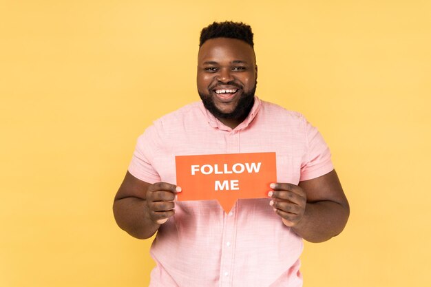 Happy man blogger holding card with follow me inscription looking at camera with toothy smile