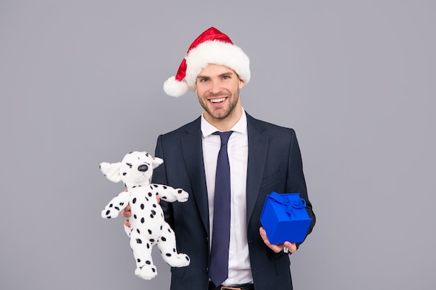 비즈니스 정장과 산타클로스 모자를 쓴 행복한 남자는 선물 상자와 장난감, 정리를 들고 있습니다.