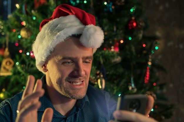 Uomo felice che chiama gli amici per natale utilizzando lo smartphone che festeggia il nuovo anno a casa