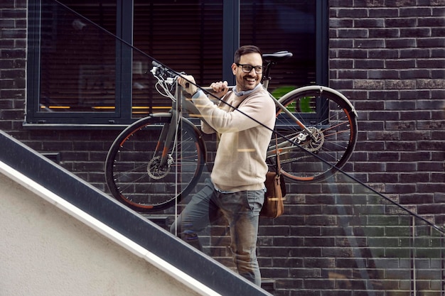 A happy man carries bicycle on the stairs outside