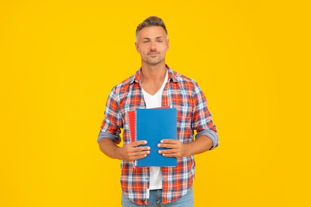 Happy man in casual holding school books yellow background teacher