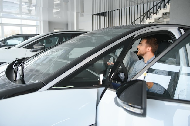 幸せな男が自動車ディーラーで新しい電気自動車を選びます エコロジカルな自動車を買うというコンセプト