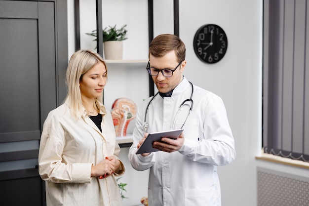 Happy man doctor showing tablet woman patient in clinic office interior Health care visit to family therapist treatment of illness and medical help