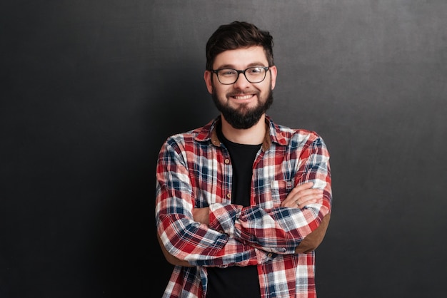 Happy man dressed in shirt in a cage and wearing glasses standing on chalkboard with arms crossed