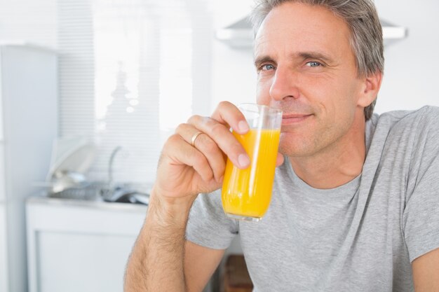 Uomo felice che beve il succo d'arancia in cucina