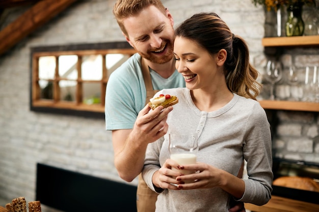 Happy man feeding his girlfriend in the morning in the kitchen