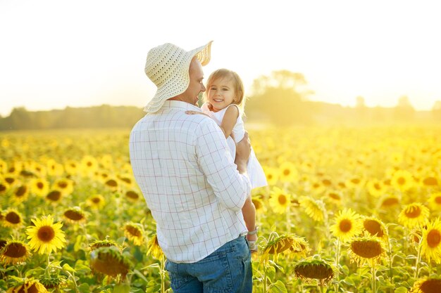 Happy man and girl in a field of sunflowers at sunset