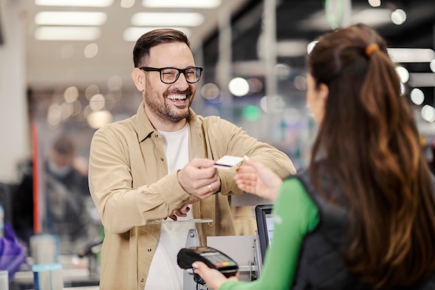 A happy man giving credit card to cashier in supermarket and paying check