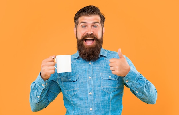 Happy man giving thumbs up holding coffee mug yellow background copy space