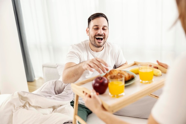 妻が居心地の良い家に連れてきたベッドで朝食を食べる幸せな男性