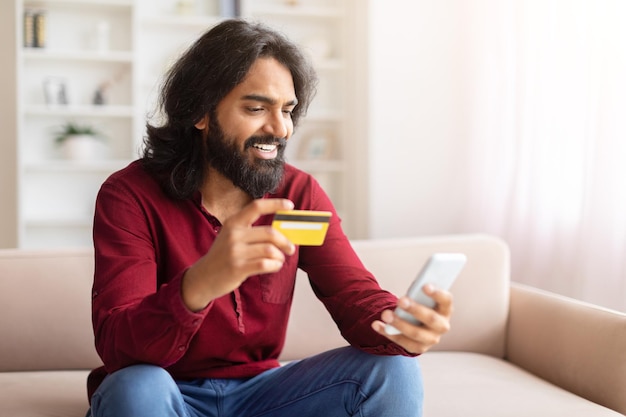 Happy man holding card and phone at home