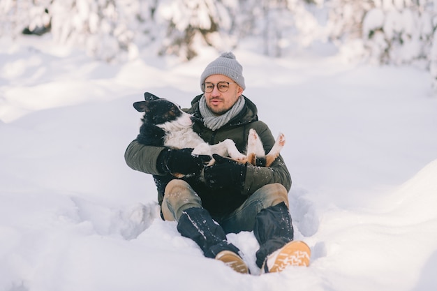 雪に覆われた森で素敵な犬を手に持って幸せな男。