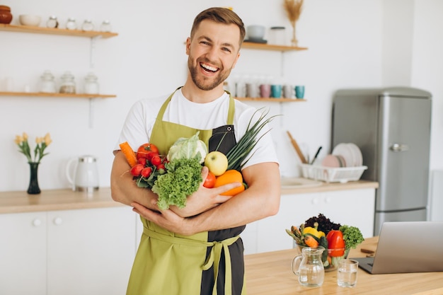 Счастливый мужчина держит дома много разных свежих овощей на кухне