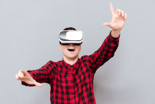 Happy Man in rood shirt in virtual reality-apparaat met camerabord met open mond. Geïsoleerde grijze achtergrond