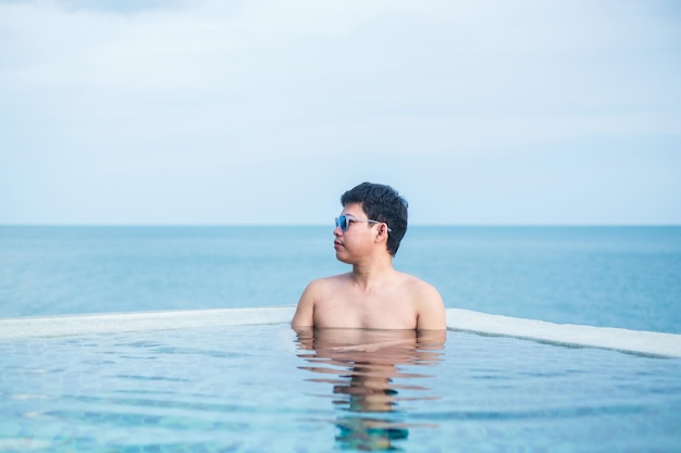 Happy man in infinity pool at luxury hotel against ocean front. young male enjoy in tropical resort. Relaxing, summer,  travel, holiday, vacation and weekend concept
