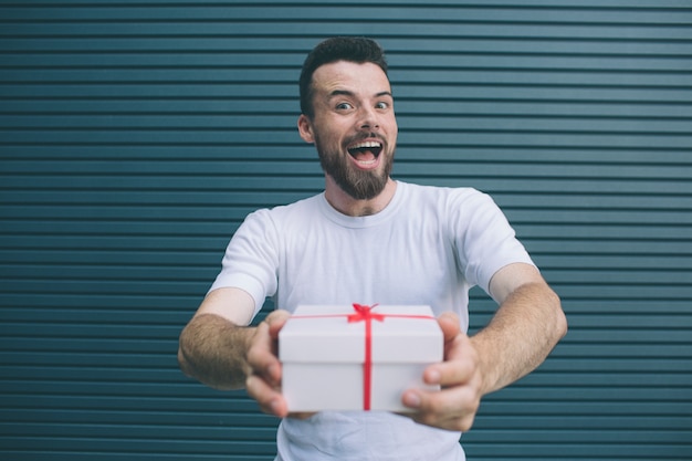 Happy man is holding present in hands. He is looking on camera and smiling. Guy is excited. Isolated on striped 