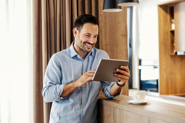 A happy man is standing at home and reading an email on tablet