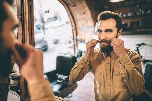 Happy man is touching his moustache with both hands. He is proud of it.