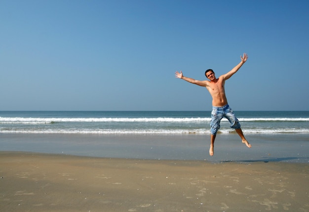 海のビーチでジャンプする幸せな男