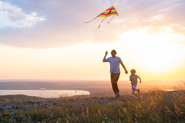 Happy man and kid boy father and son run with kite in nature at sunset