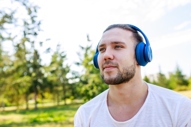 Photo happy man listening music with headphone in white blazer outdoor in summer park