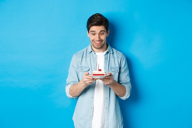 Happy man looking at birthday cake and making with, standing over blue background