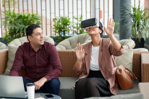 Happy man looking at coworker in VR headset enjoying playing videogame he created