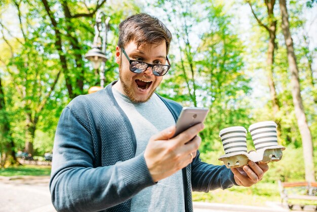 Happy man looking on phone with popeyed view coffee to go in hands