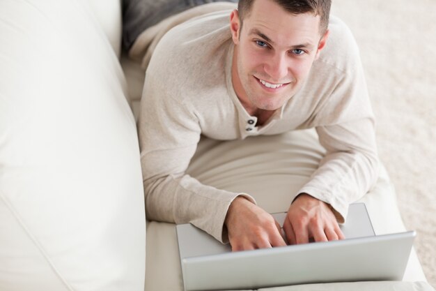 Happy man lying on a couch with a notebook