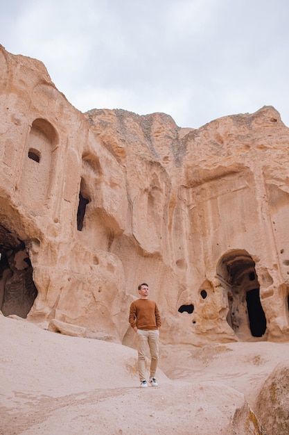 Happy man outdoor on background of ancient cave formations in Cappadocia, Turkey. The Monastery is one of the largest religious buildings.