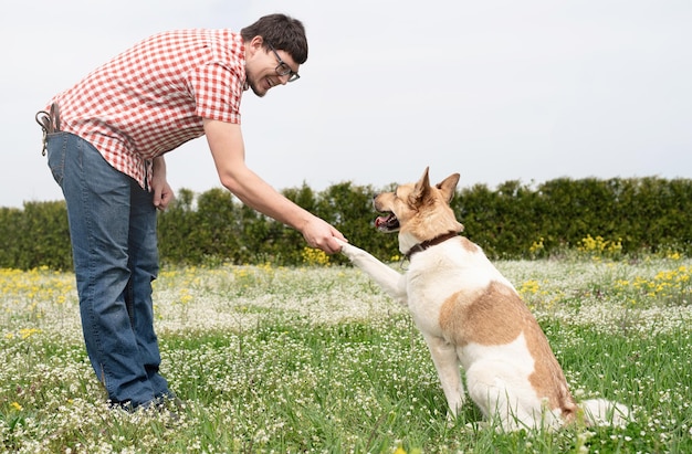 幸せな男は緑の草の上で混合品種の羊飼いの犬と遊ぶ