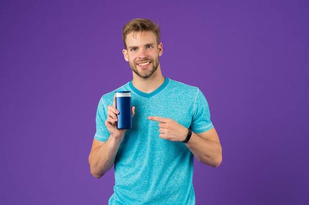 Happy man point finger at gel tube on violet background Bearded man smile with shampoo bottle Skincare and hair care Health and healthcare Cosmetic for spa and bath or shower copy space