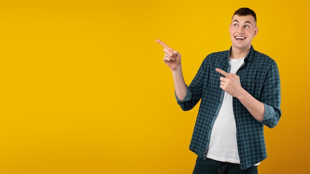 Happy man pointing fingers aside at free space yellow background