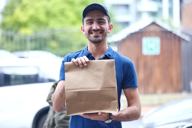 Happy man portrait and paper bag for delivery supply chain or transport of goods in courier service Friendly male person with parcel package or cargo for online order purchase or ecommerce