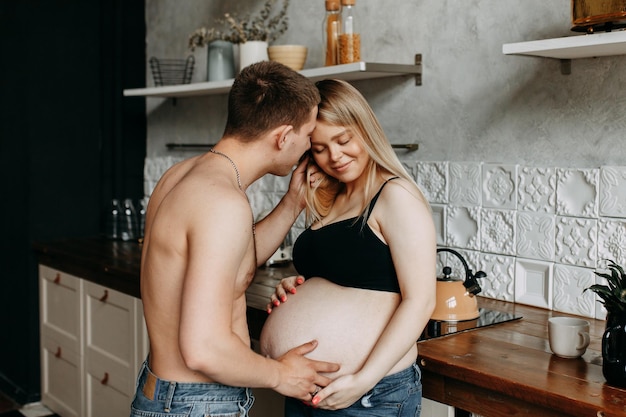 A happy man and a pregnant woman hug and kiss in the kitchen in a cozy house
