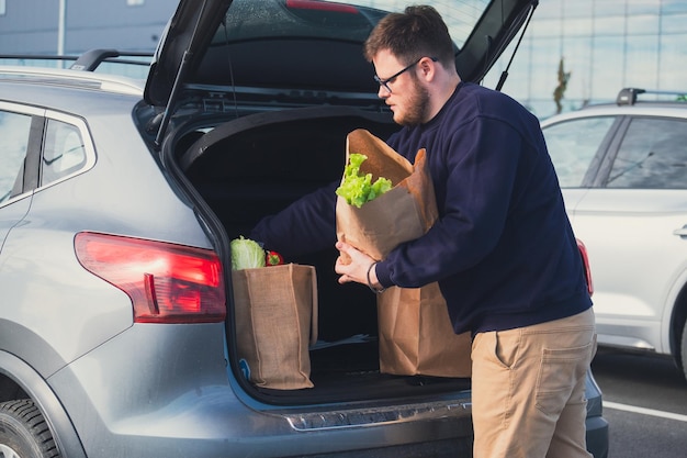 happy man put groceries bag in car trunk mall parking place