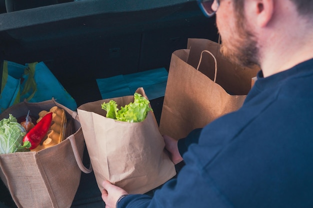 happy man put groceries bag in car trunk mall parking place