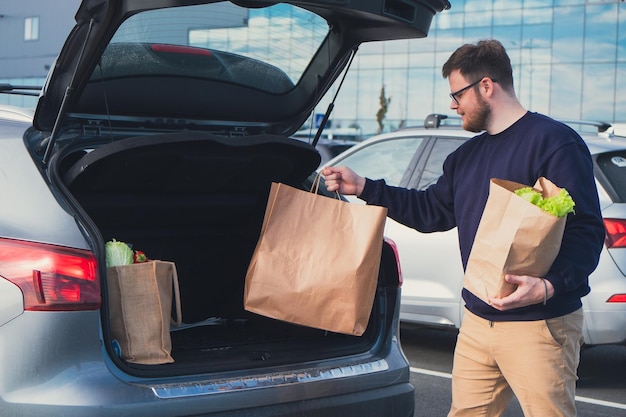 幸せな男が買い物袋を車のトランクに置いた ショッピングモールの駐車場