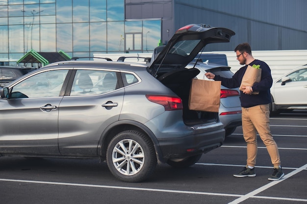 happy man put groceries bag in car trunk mall parking place